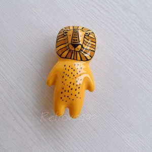 May include: A yellow ceramic figurine of a lion with black details. The lion has a striped mane and a spotted body.