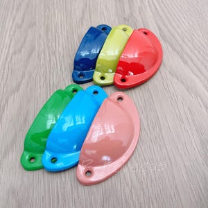 Könnte beinhalten: Sortiment an bunten Metall-Schubladengriffen in verschiedenen Blautönen, Grün, Gelb, Rot und Rosa. Diese dekorativen Schrankgriffe haben die Form von Halbkreisen.