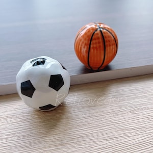 Może przedstawiać: Dwa ceramiczne ozdoby w kształcie piłek sportowych, biała i czarna piłka nożna oraz pomarańczowa i czarna piłka do koszykówki.