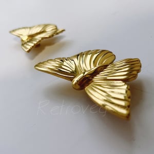 May include: Two gold-toned butterfly-shaped metal embellishments. The butterflies have a detailed, textured design.