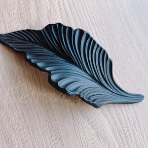 Könnte beinhalten: Schwarzer, blattförmiger Schrankgriff mit detailliertem, strukturiertem Design.