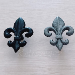 May include: Two decorative metal fleur-de-lis drawer pulls, one black and one silver.