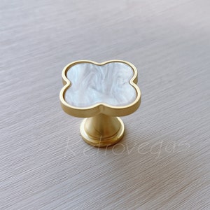 May include: A gold-toned cabinet knob with a white, marbled, four-leaf clover design.