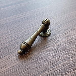 May include: A vintage-style, antique gold-toned cabinet pull with a rounded handle and a decorative base.