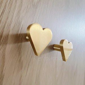 Peut inclure: Deux crochets en forme de cœur dorés. Le crochet le plus grand est à gauche et le plus petit à droite.