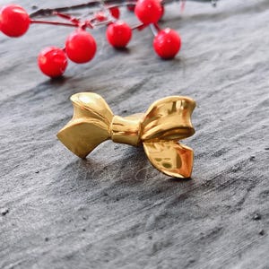 May include: A gold-coloured bow-shaped cabinet knob or drawer pull.