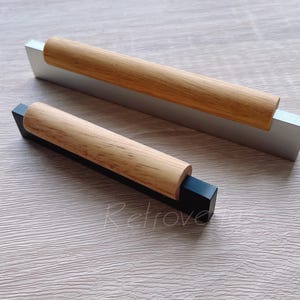 May include: Two wooden cabinet pulls with black and silver bases. The pulls are made of natural wood and have a simple, modern design.