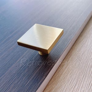 May include: A square-shaped, brushed gold cabinet knob.