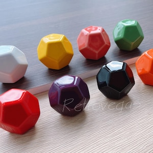 Peut inclure: Collection de huit objets décoratifs géométriques et à facettes multiples, de couleurs variées : blanc, jaune, rouge, vert, orange, violet et noir. Les objets sont disposés sur une surface en bois, mettant en valeur leur finition brillante et leurs formes uniques.