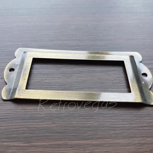 以下が含まれることがあります： ラベルを入れるための長方形の開口部のある真鍮製の引き出しラベル。ラベルはわずかに使い古した仕上げになっています