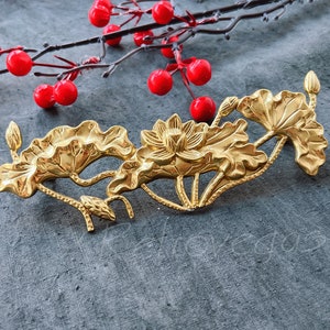 Op de afbeelding: Een goudkleurig decoratief stuk met lotusbloem en bladeren. Het bloemmotief is gedetailleerd met een centrale bloem en omringende bladeren. Rode bessen op een tak staan op de achtergrond. Voor interieurdecoratie.