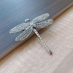 May include: Silver dragonfly cabinet knob with detailed wings and a textured finish.
