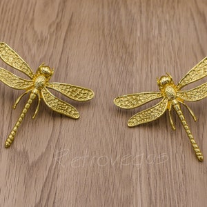 May include: Two gold-toned dragonfly earrings with detailed wings and a textured finish.