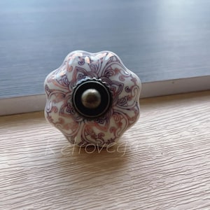 Może przedstawiać: Biały ceramiczny gałka do szafki z kwiatowym wzorem w odcieniach różowego i brązowego. Gałka ma okrągłą, brązową podstawę.