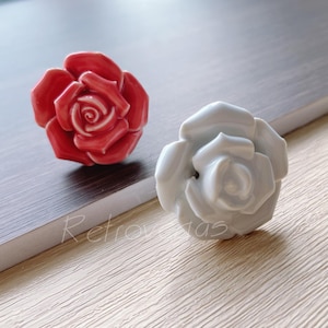 Pode incluir: Dois puxadores de gaveta de cerâmica em forma de rosa, um vermelho e outro branco.