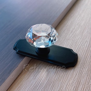 Könnte beinhalten: Ein schwarzer Schrank-Knopf mit einem durchsichtigen, diamantförmigen Kristallgriff.