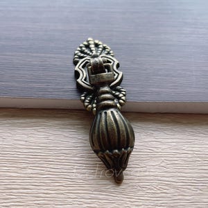 Op de afbeelding: Een decoratieve antieke stijl kastknop met een geribbeld ontwerp en sierlijke details. De knop is gemaakt van metaal en heeft een donker bronzen afwerking.