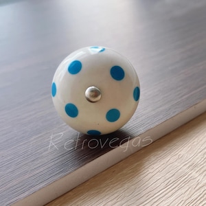 Peut inclure: Bouton de porte en céramique blanche avec des pois bleus. Le bouton a une vis en métal argenté au centre.