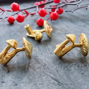 Könnte beinhalten: Drei goldfarbene, pilzförmige Schrankknöpfe. Die Knöpfe sind mit einer strukturierten Pilzkappe und einem Stiel verziert.