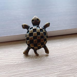 May include: A bronze turtle drawer pull with a checkered pattern on its shell.