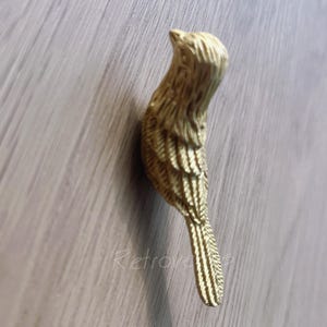 May include: Gold-toned metal bird-shaped cabinet knob or drawer pull. The bird has a detailed design with textured feathers.