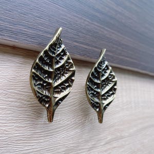 May include: Two gold leaf-shaped cabinet knobs with a detailed textured design.