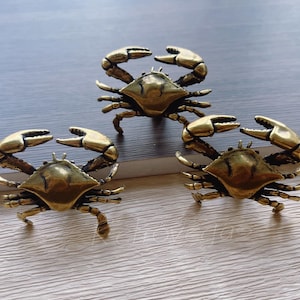 Peut inclure: Trois figurines de crabe en laiton avec des pinces et des pattes détaillées. Les crabes sont placés sur une surface claire, avec un fond gris foncé. Les figurines de crabe ont un aspect vintage et antique.