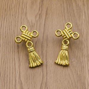 May include: Two gold-tone tassel charms with a knot design. The tassels are approximately 2.5 cm long.