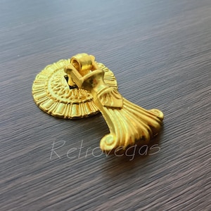 Puede incluir: Tirador de cajón decorativo dorado con un diseño floral y un tirador estilizado y adornado.