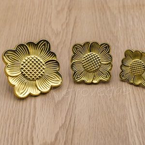 May include: Three gold-coloured metal flower-shaped drawer pulls in different sizes.