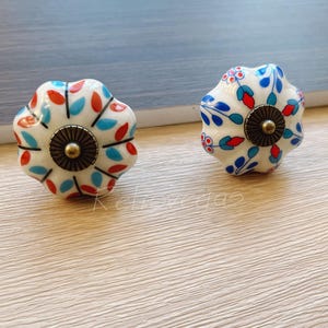 May include: Two white ceramic cabinet knobs with a floral design in blue, red, and green. The knobs have a gold metal base.