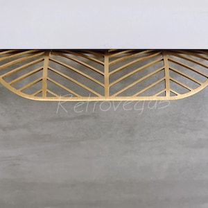 May include: A gold-colored, leaf-shaped drawer pull with a geometric design. The pull is mounted on a gray surface, with a white surface above. The word "Retrovegas" is visible in the image.