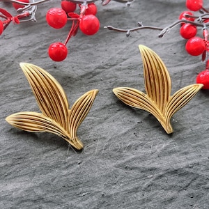 May include: A pair of gold leaf-shaped earrings. The earrings are made of metal and have a textured surface.