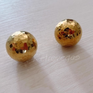 May include: Two gold-coloured, round, hammered metal earrings.