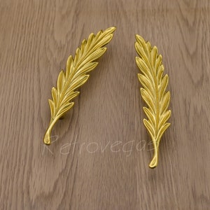 Puede incluir: Dos tiradores de armario en forma de hoja de oro. Los tiradores son de metal y tienen un diseño detallado.