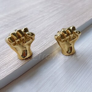 May include: Two gold-colored metal drawer pulls shaped like fists.