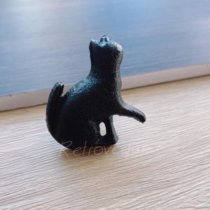 May include: Black cast iron cat figurine. The cat is sitting up with its tail curled around its legs. It is looking up and has a playful expression.