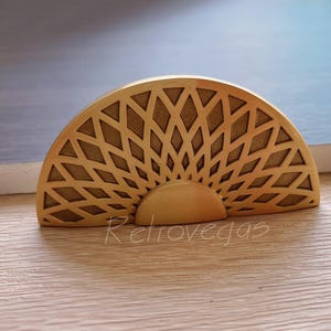 Könnte beinhalten: Ein goldfarbener Metall-Schrankgriff mit geometrischem Design. Der Griff ist halbkreisförmig mit einem erhöhten, massiven Mittelteil.