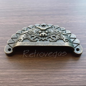May include: A decorative bronze drawer pull with a dragon design. The pull is shaped like a half-circle and has a scalloped edge.