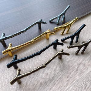 Op de afbeelding: Assortiment van zes verschillende takvormige kastgrepen in zwart, goud en zilver. De grepen hebben een rustieke, natuurlijke uitstraling.