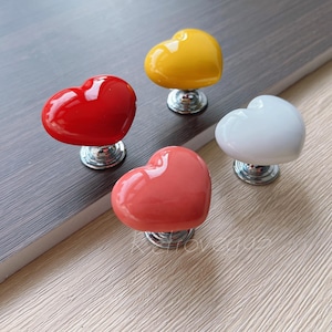 May include: Four heart-shaped ceramic cabinet knobs in red, yellow, white, and pink. Each knob has a silver base.