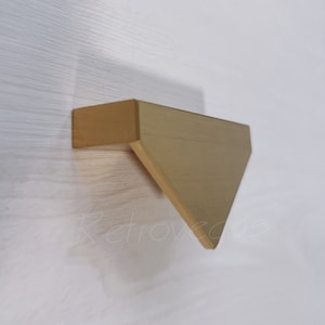 Peut inclure: Poignée de meuble triangulaire en or avec une finition brossée.