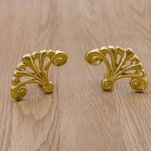 May include: Two gold-coloured metal decorative drawer pulls with a fan-shaped design.