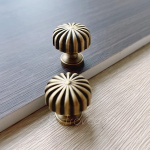 May include: Two antique brass cabinet knobs with a fluted, sunburst design. The knobs are round and have a raised centre.