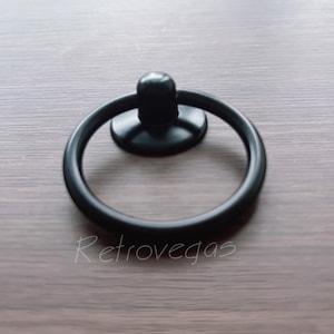 Può includere: Maniglia ad anello nero con base rotonda. La maniglia è in metallo e ha una finitura liscia.