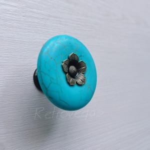 Può includere: Un pomello rotondo per armadi di colore blu turchese con un design floreale in metallo decorativo.
