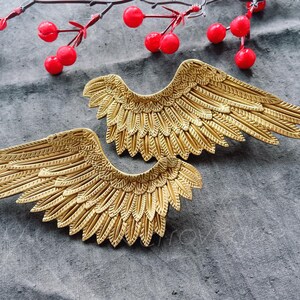 Puede incluir: Un par de alas de ángel de metal dorado con un diseño de plumas detallado. Las alas están dispuestas de forma simétrica, con las puntas de las alas apuntando hacia afuera.
