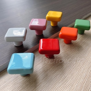 Puede incluir: Siete pomos de armario cuadrados de cerámica en varios colores, incluyendo blanco, azul claro, rosa, rojo, naranja, verde y amarillo.