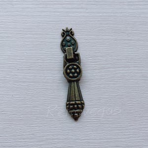 May include: A vintage-style, ornate, bronze-colored drawer pull with a decorative floral design.