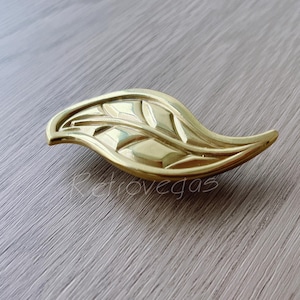 May include: A gold leaf-shaped cabinet pull with a detailed design.